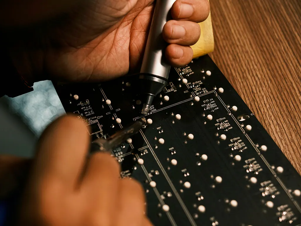Hands soldering a circuit board on a timber desk in warm light