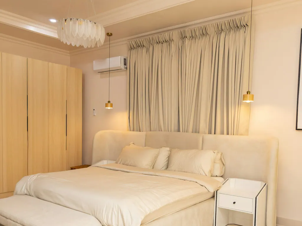 A calm cream bedroom with a wall-mounted split air conditioner above the curtains