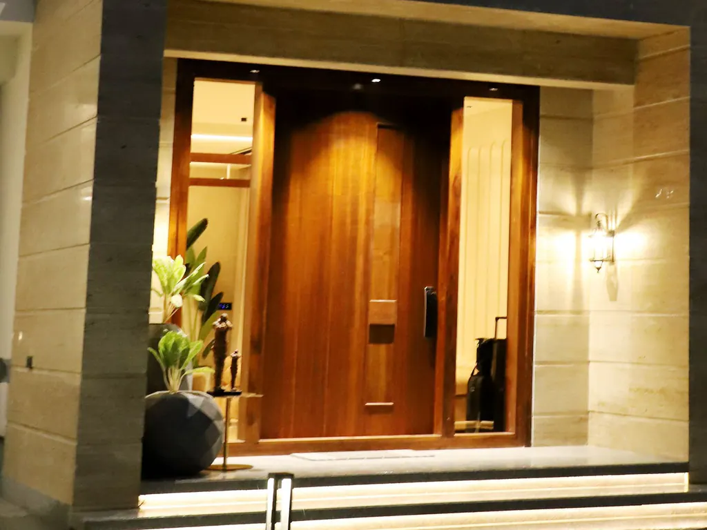 A teak front door with a slim digital lock, lit steps and garden lights at dusk