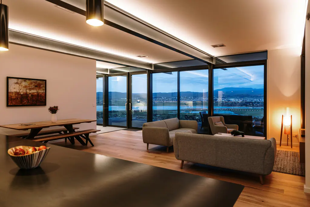 Open-plan living room at dusk with cove lighting, a pendant and a floor lamp glowing against tall windows