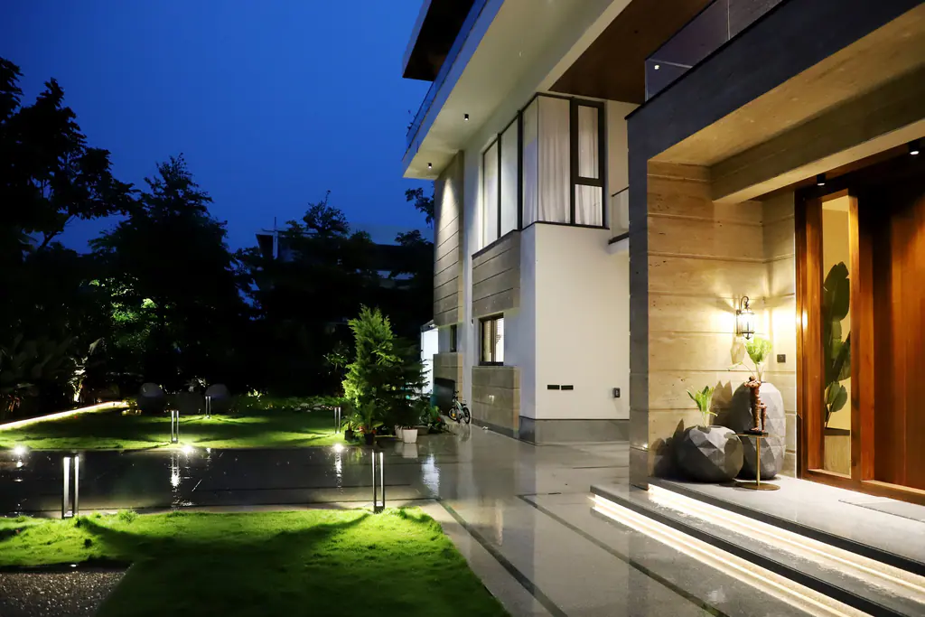 A modern home at blue hour: lit steps up to a warm-lit entrance, garden lights along the lawn and a softly glowing facade