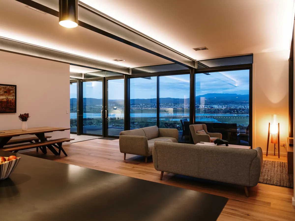 Open-plan living room at dusk with cove lighting, a pendant and a floor lamp glowing against tall windows