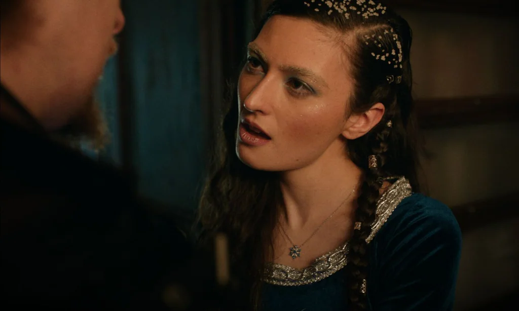 Film still from The Morningstars: a woman with braided hair and a jewelled headpiece speaks in warm candlelight