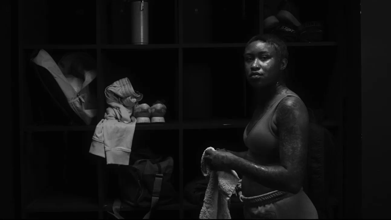Film still from Piroba, in near black and white: a boxer holding a towel stands by the lockers after a fight